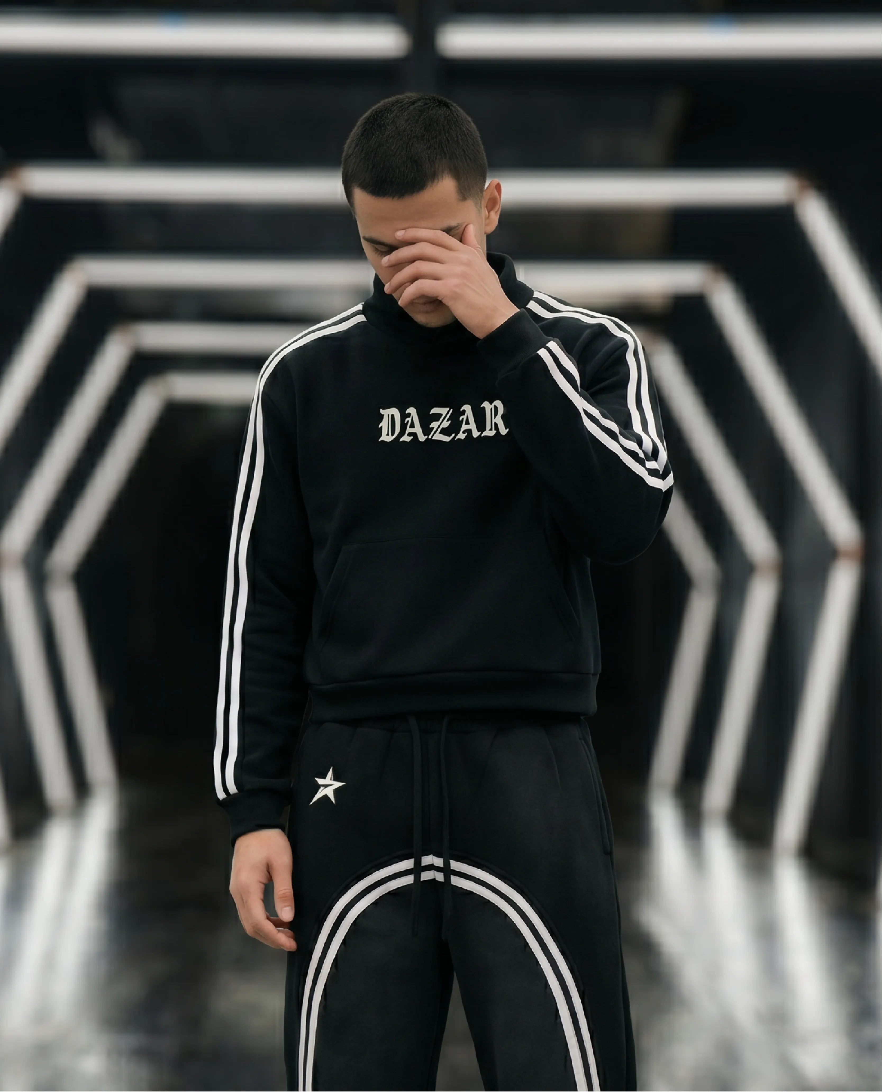 Person wearing a black tracksuit with 'DAZAR' branding in a geometric background